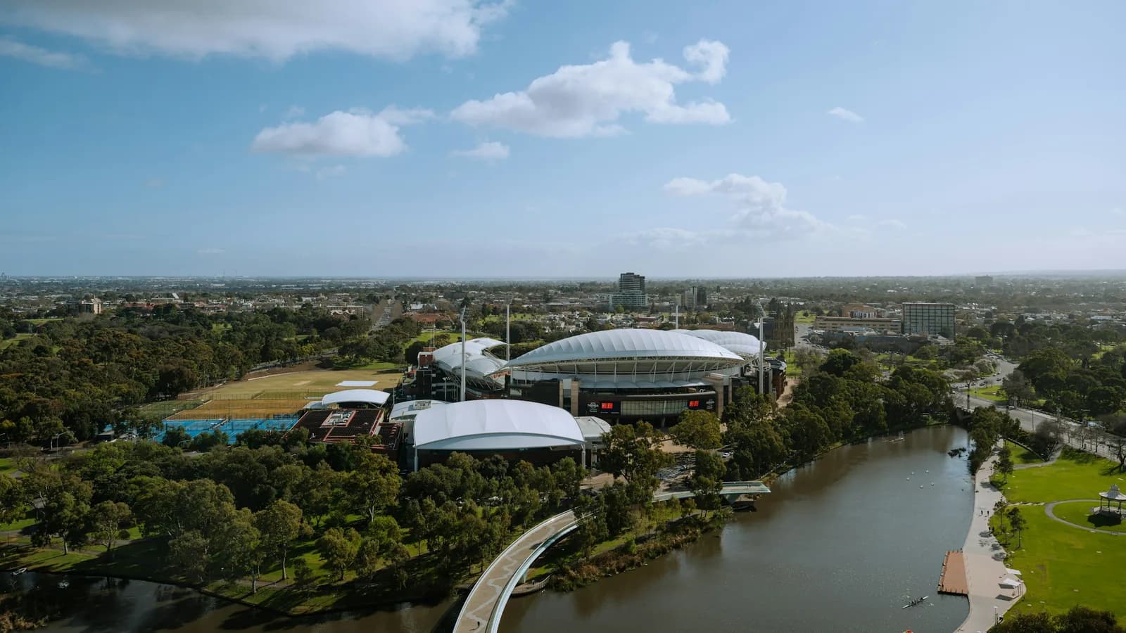 Aerial photograph of Adelaide Oval beside the River Torrens, with the parklands, North Adelaide and the suburbs beyond.